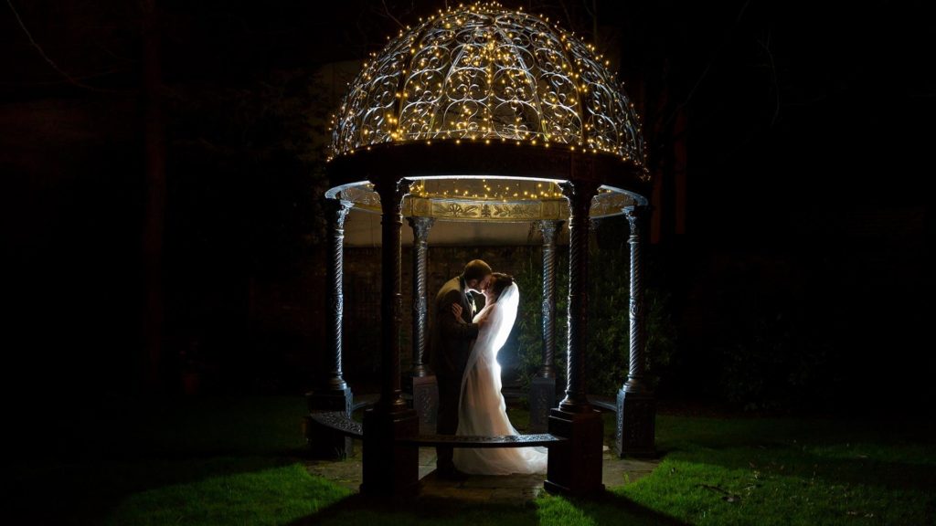 Romantic couple embraces under illuminated garden gazebo at The Clarendon hotel, perfect for weddings and special events.