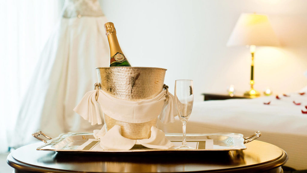 Elegant room with champagne and glass on silver tray, soft lighting and luxurious bedding at The Clarendon.