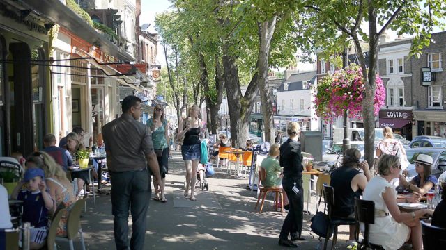Guests enjoying vibrant outdoor dining on a sunny street lined with trees and flowers, near The Clarendon Hotel.