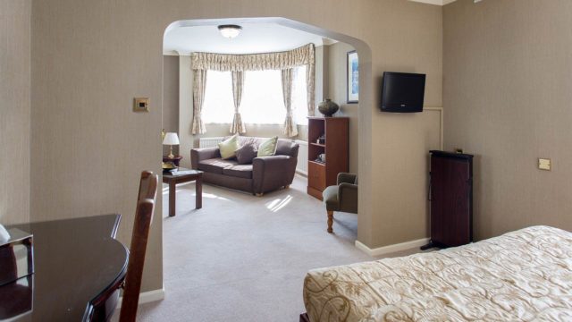 Spacious hotel room with elegant decor, cosy sofa, elegant drapes, and flat-screen TV. Ideal for a relaxing stay.