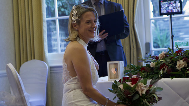 Bride smiles at indoor wedding ceremony with elegant decor and floral arrangements at The Clarendon Hotel.
