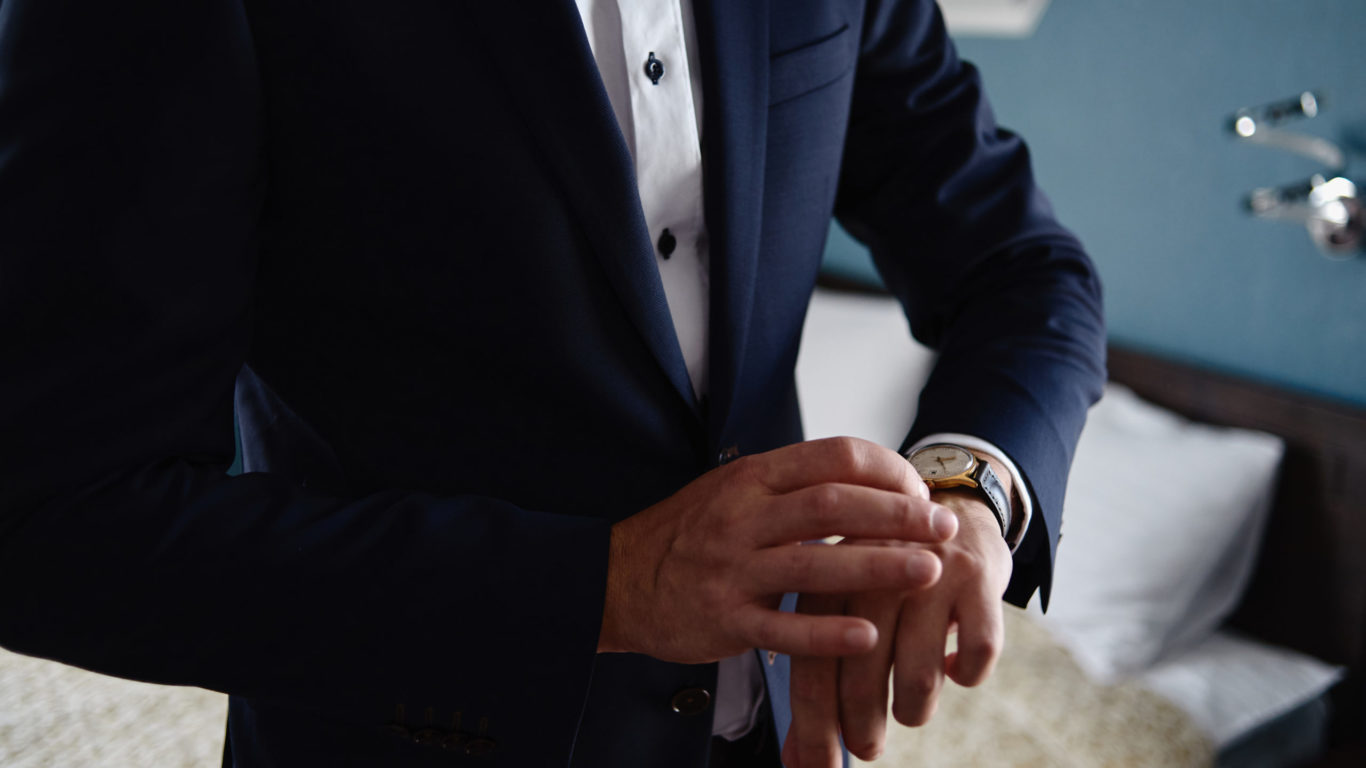 Businessman looking at watches on his hand indoors, copy space. Man in blue suit checking time from luxury wristwatches. Watch on hand. Groom wedding preparation