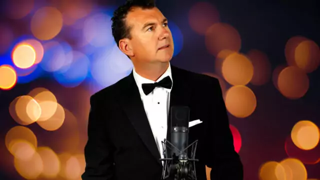 Dapper man in tuxedo sings with vintage microphone, colourful bokeh background. Perfect for elegant hotel events.