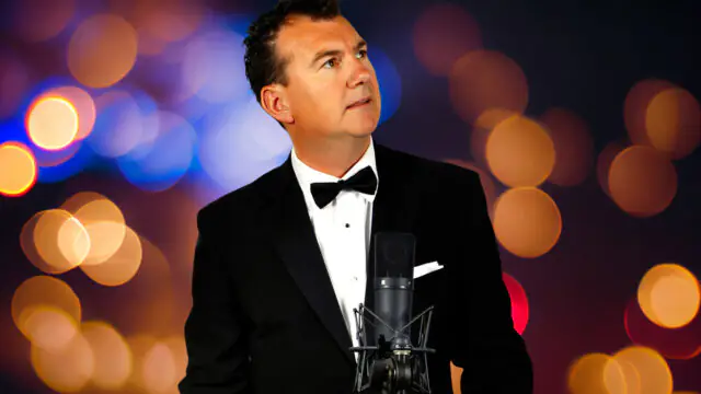 Dapper man in tuxedo sings with vintage microphone, colourful bokeh background. Perfect for elegant hotel events.