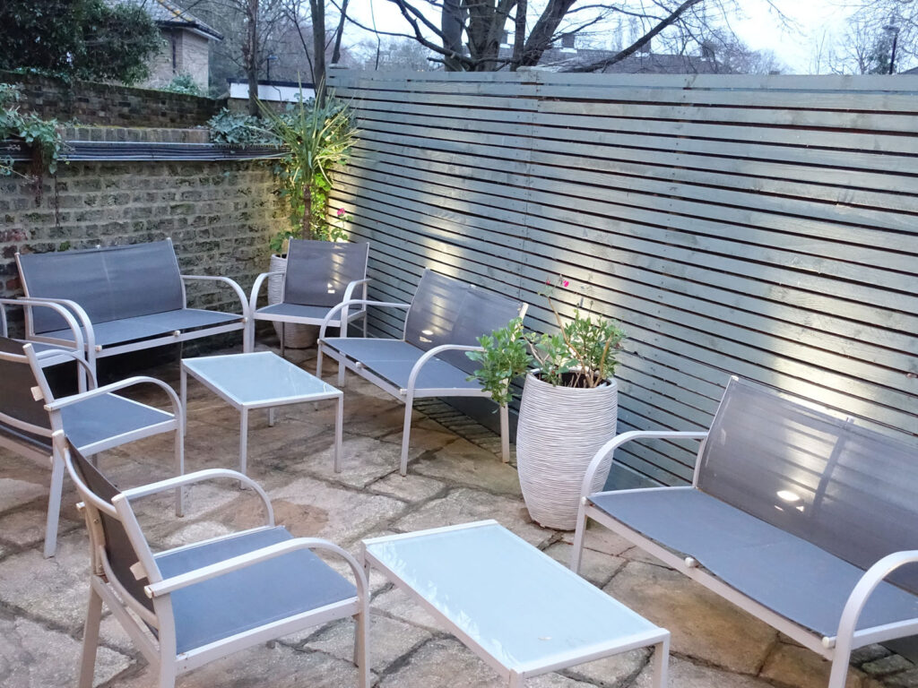 Tranquil Courtyard Seating Area Modern outdoor seating area with cosy chairs, wooden fencing, and soft lighting at The Clarendon's quiet courtyard.