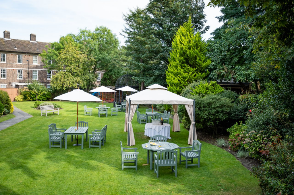 Charming Hotel Garden Oasis Enjoy The Clarendon's lush garden with outdoor seating, parasols, and serene views, perfect for relaxing or dining al fresco.