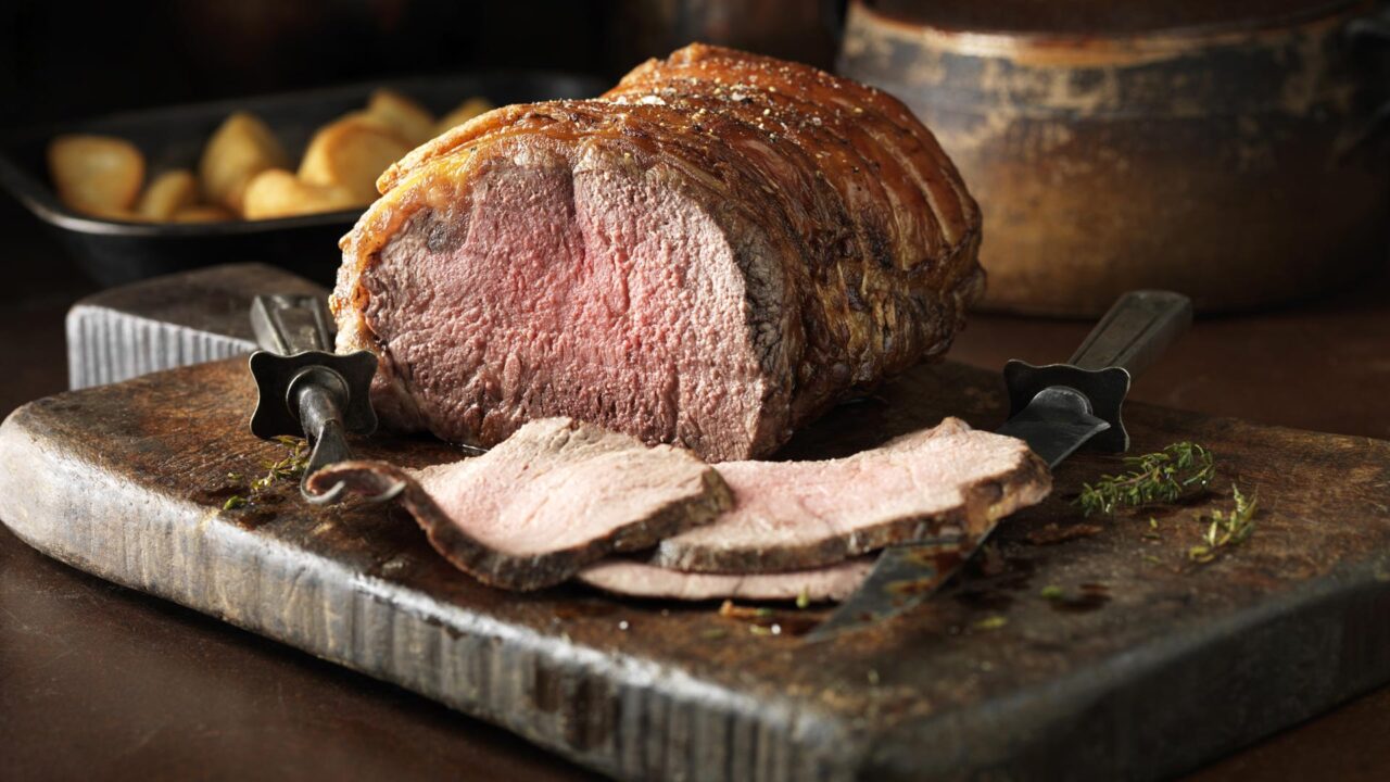 Succulent roast beef on wooden board, garnished with herbs, inviting dining experience at The Clarendon Hotel.