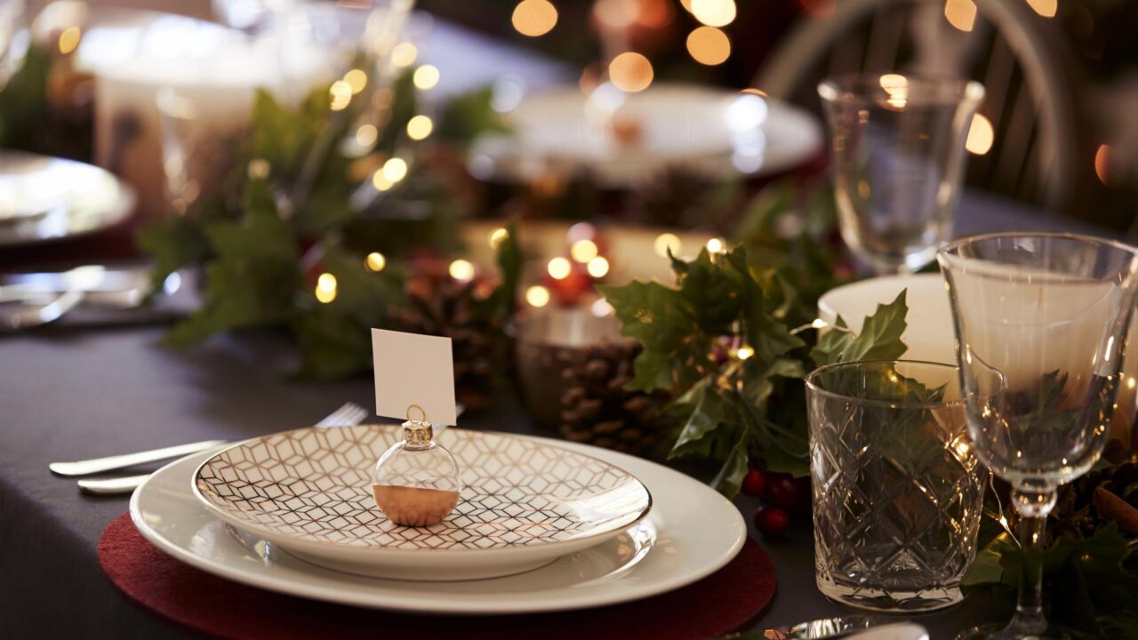 Elegant holiday dining setup with intricate plates, twinkling lights, festive greenery, and glasses at The Clarendon Hotel.