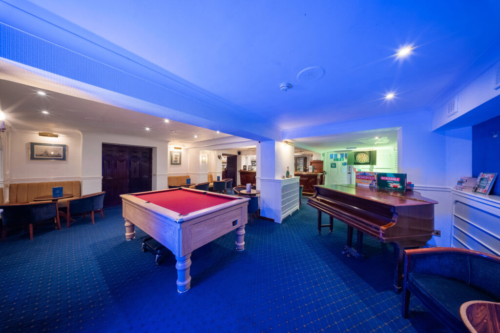 Elegant leisure room with pool table, piano, dartboard, and cosy seating at The Clarendon, perfect for relaxation.