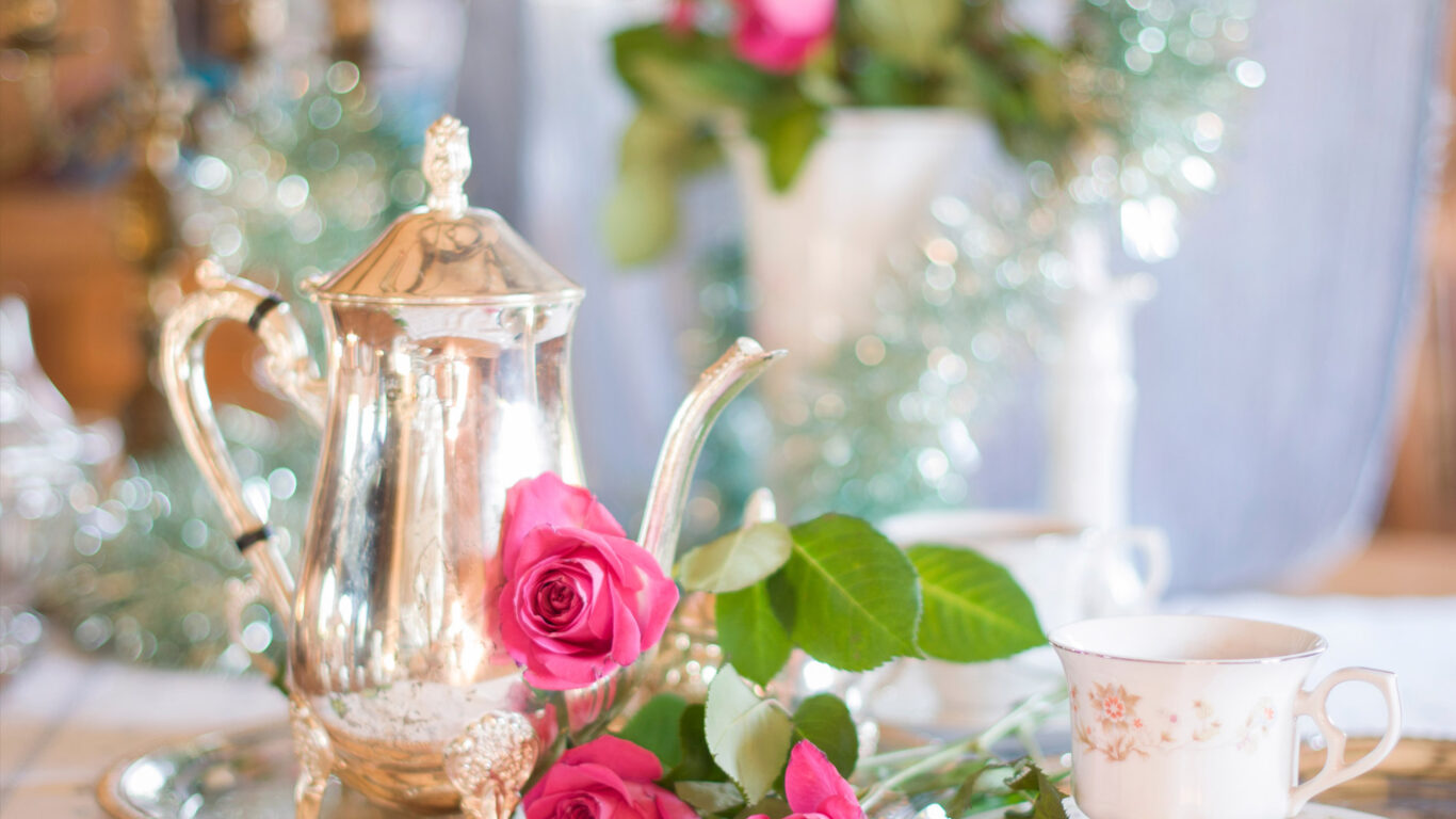 Elegant silver teapot, roses, and fine china for afternoon tea at The Clarendon, promising luxury and refined relaxation.