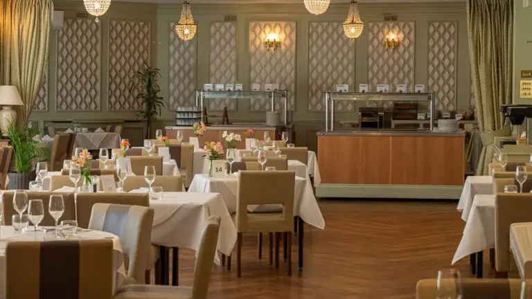 Elegant Clarendon Hotel dining room with chandeliers, cosy seating, floral centrepieces, and buffet area. Perfect for fine dining.