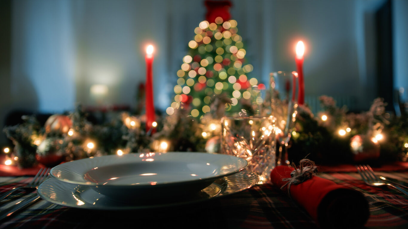 Festive table setting at The Clarendon with candles, elegant dinnerware, and a sparkling Christmas tree, inviting holiday ambiance.