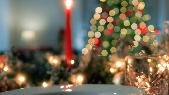 Festive dining setup with elegant plates, glowing Christmas tree, and candlelight, inviting warmth at The Clarendon hotel.