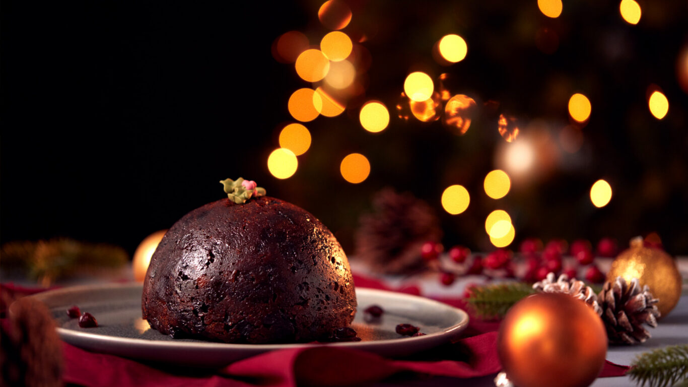 Festive Christmas pudding on a plate with glowing bokeh lights, creating a warm holiday atmosphere at The Clarendon Hotel.